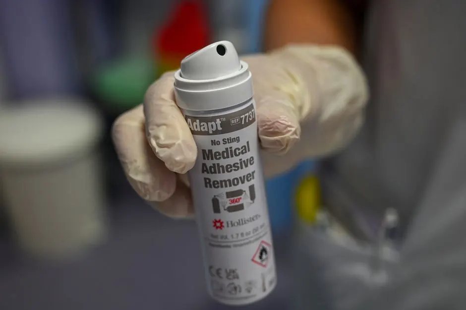 A nurse wearing gloves shows a can of medical adhesive remover in a clinical setting.